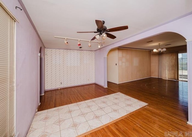 empty room with arched walkways, wood finished floors, a ceiling fan, and wallpapered walls