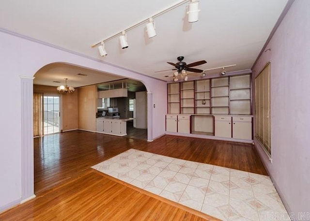 unfurnished living room with track lighting, arched walkways, and wood finished floors