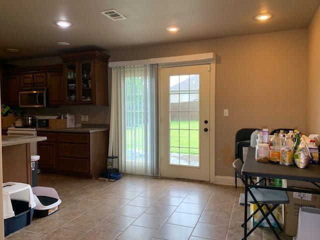 4709 Summit Rdg, Jonesboro, AR 72404 - kitchen with stainless steel microwave, light countertops, glass insert cabinets, recessed lighting, and light tile patterned floors