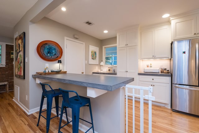 6709 Waverly Dr, Little Rock, AR 72207 - kitchen with freestanding refrigerator, dark countertops, light wood-type flooring, a breakfast bar area, and recessed lighting
