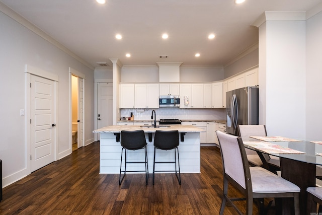 313 Parker St, North Little Rock, AR 72114 - kitchen featuring appliances with stainless steel finishes, a center island with sink, tasteful backsplash, dark wood-style floors, and ornamental molding