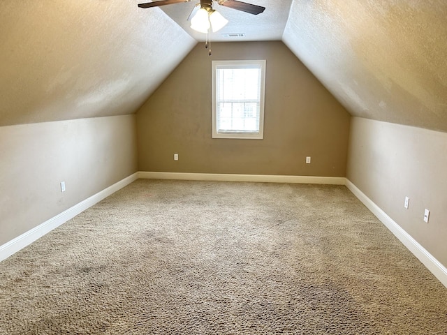 additional living space with a textured ceiling, ceiling fan, carpet floors, vaulted ceiling, and baseboards