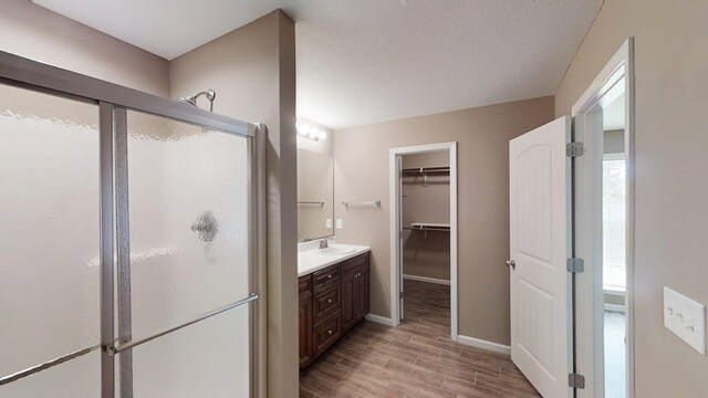 bathroom with a stall shower, wood finished floors, vanity, baseboards, and a spacious closet