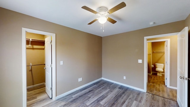 unfurnished bedroom featuring wood finished floors, a walk in closet, baseboards, and a closet