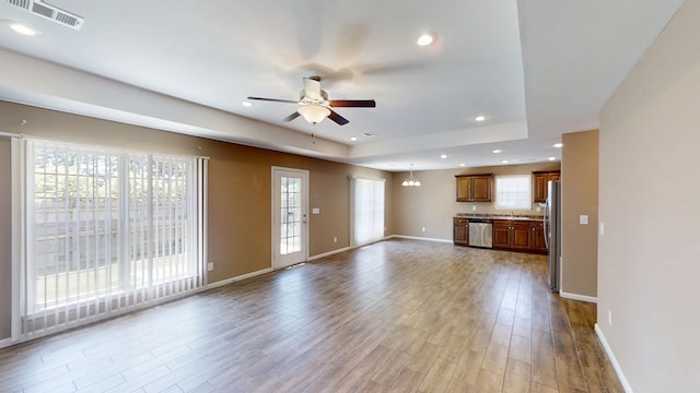 unfurnished living room featuring a ceiling fan, recessed lighting, baseboards, light wood finished floors, and a tray ceiling