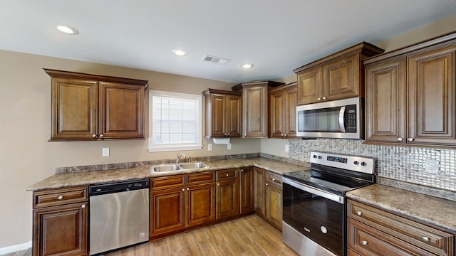 kitchen featuring appliances with stainless steel finishes, a sink, light wood finished floors, tasteful backsplash, and recessed lighting
