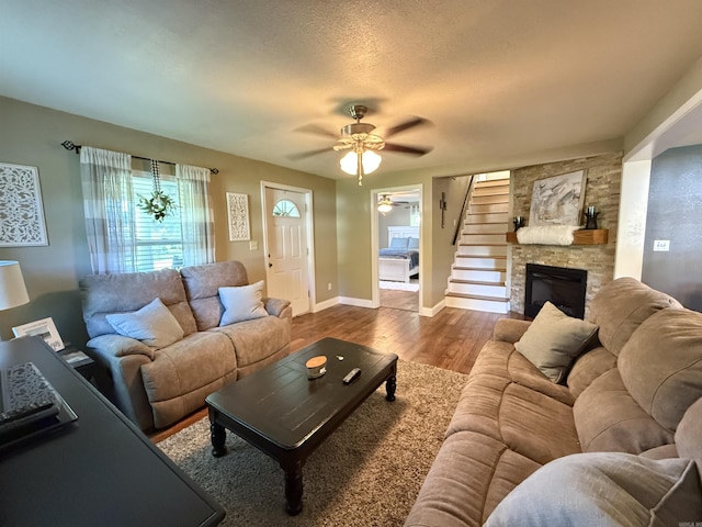 507 E Bruce St, Piggott, AR 72454 - living room with ceiling fan, dark wood-type flooring, a stone fireplace, a textured ceiling, and baseboards