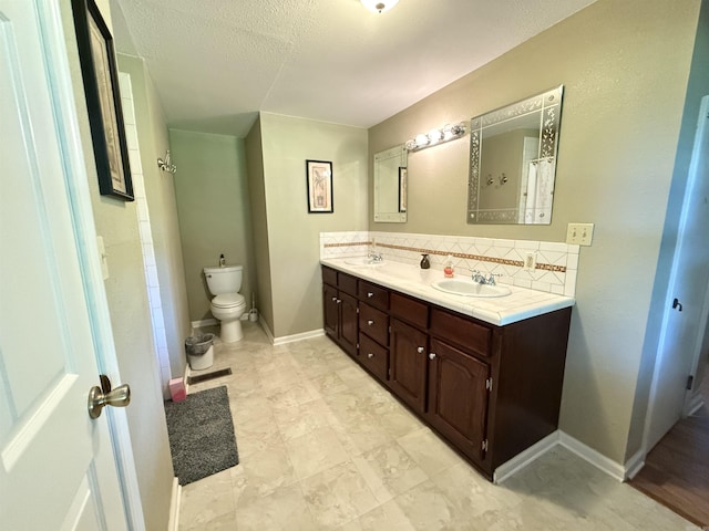 507 E Bruce St, Piggott, AR 72454 - bathroom featuring double vanity, tasteful backsplash, toilet, baseboards, and a textured ceiling