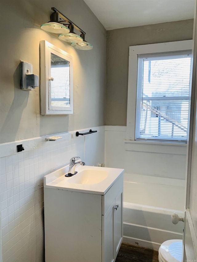 bathroom featuring vanity, toilet, a tub, wainscoting, and tile walls