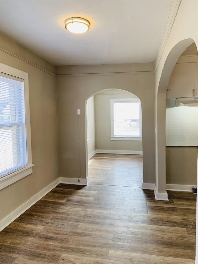 spare room featuring arched walkways, wood finished floors, and baseboards