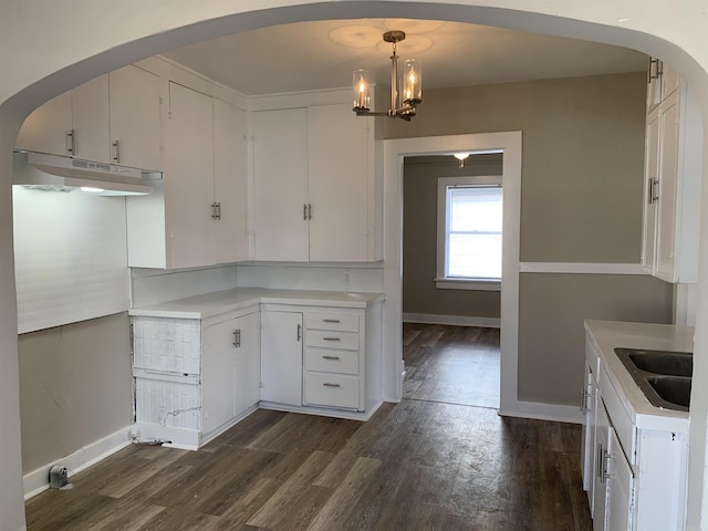 kitchen featuring under cabinet range hood, arched walkways, a sink, and dark wood finished floors