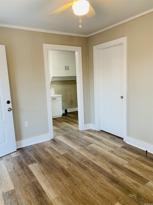 empty room with a ceiling fan, wood finished floors, ornamental molding, and baseboards