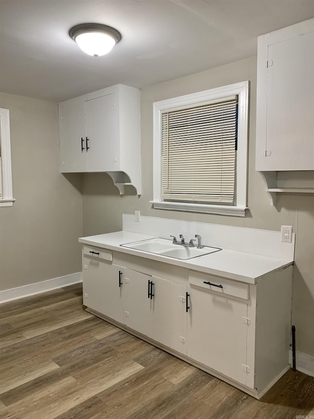 kitchen with a sink, light wood finished floors, light countertops, white cabinetry, and baseboards