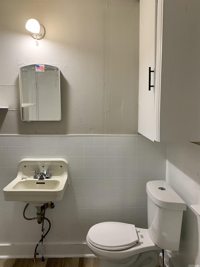 half bath featuring tile walls, toilet, a sink, and wood finished floors