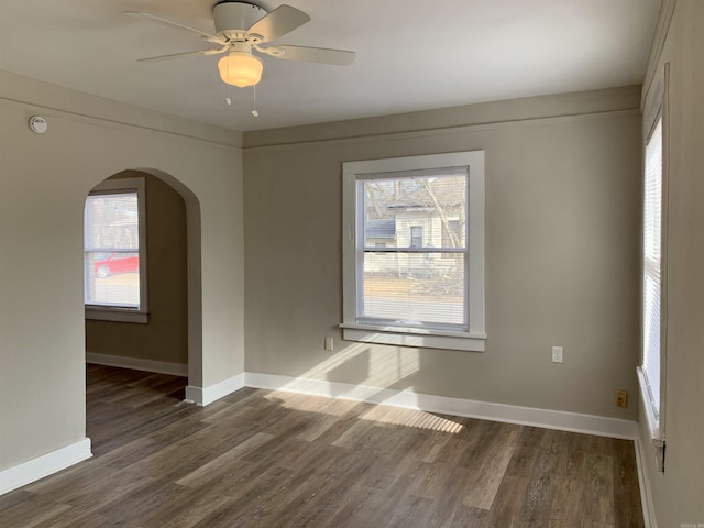 spare room with arched walkways, dark wood-type flooring, baseboards, and healthy amount of natural light