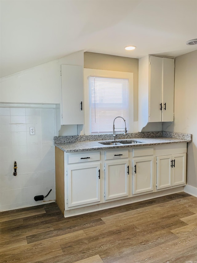 kitchen with a sink, white cabinetry, wood finished floors, light stone counters, and lofted ceiling