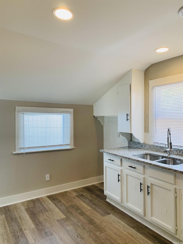 kitchen with a sink, vaulted ceiling, dark wood finished floors, light stone countertops, and white cabinetry