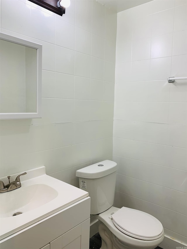 bathroom with toilet, vanity, and tile walls