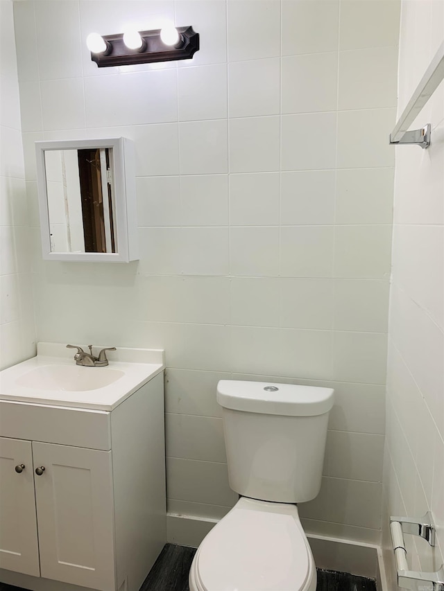 half bath with vanity, toilet, and tile walls