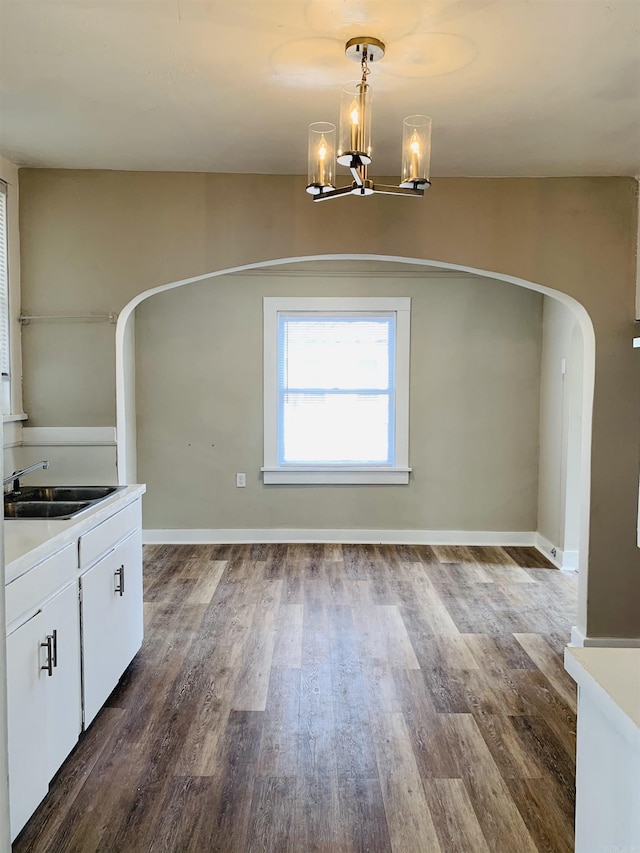 unfurnished dining area with a sink, arched walkways, dark wood-style flooring, a chandelier, and baseboards
