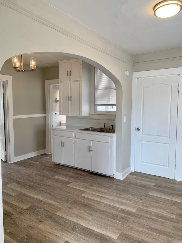 kitchen with wood finished floors, arched walkways, baseboards, and white cabinets