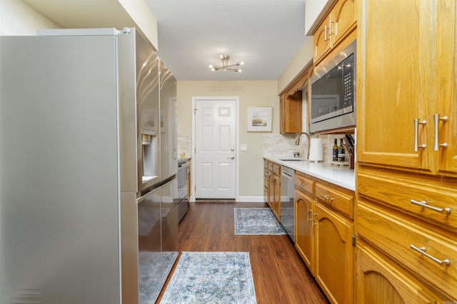 kitchen with stainless steel appliances, a sink, dark wood-type flooring, backsplash, and brown cabinets