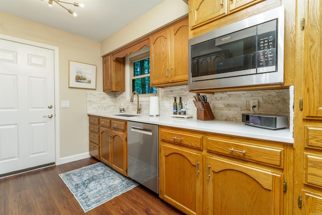 kitchen with stainless steel appliances, a sink, brown cabinets, tasteful backsplash, and dark wood-style floors