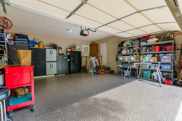 garage featuring a garage door opener and black refrigerator with ice dispenser