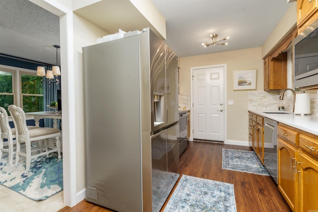 kitchen with appliances with stainless steel finishes, a chandelier, tasteful backsplash, a sink, and dark wood finished floors