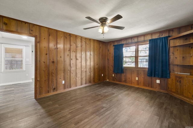 empty room featuring baseboards, a ceiling fan, wood finished floors, and wood walls