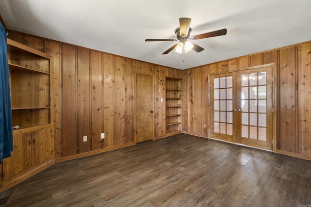 spare room with french doors, wooden walls, a ceiling fan, wood finished floors, and baseboards