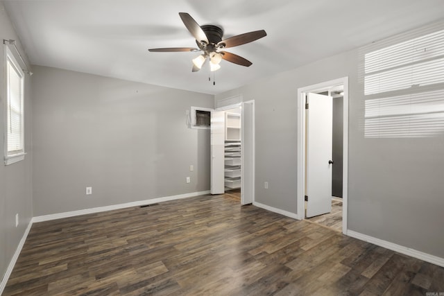 unfurnished bedroom featuring wood finished floors, baseboards, a walk in closet, and a ceiling fan