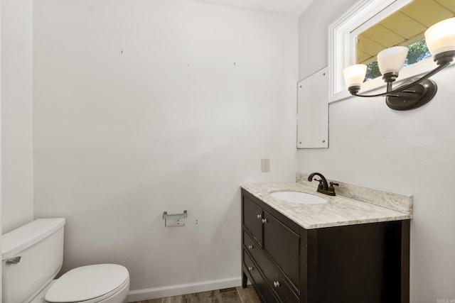 bathroom with toilet, vanity, wood finished floors, and baseboards