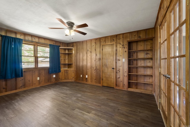 spare room with a ceiling fan, dark wood-type flooring, wooden walls, and baseboards