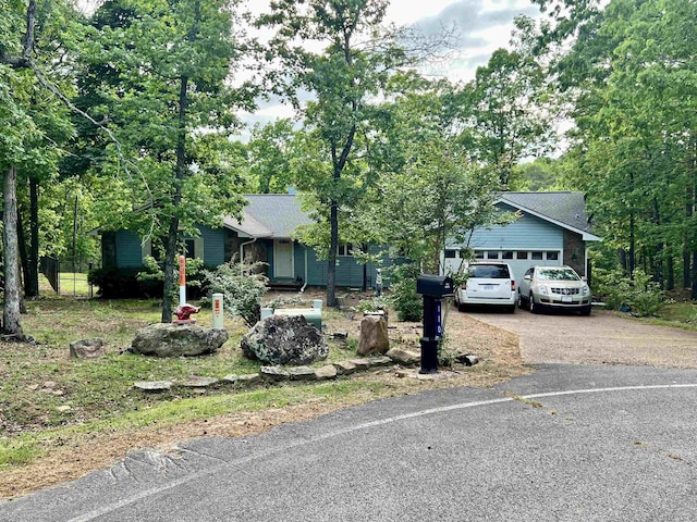 view of property hidden behind natural elements featuring driveway, a garage, and a shingled roof