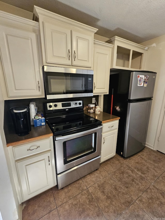 216 Plum Dr, Austin, AR 72023 - kitchen with appliances with stainless steel finishes, dark countertops, a textured ceiling, tile patterned floors, and white cabinets