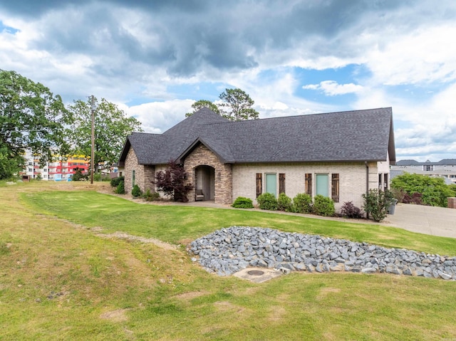view of front of home featuring roof with shingles, a front yard, and stone siding