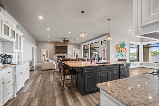 kitchen featuring a sink, a fireplace, dishwasher, a ceiling fan, and white cabinetry