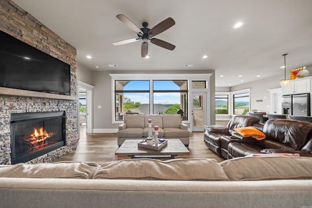 living area featuring a stone fireplace, ceiling fan, wood finished floors, recessed lighting, and baseboards