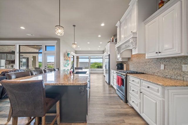 kitchen featuring stainless steel appliances, a sink, open floor plan, white cabinets, and light wood-style flooring