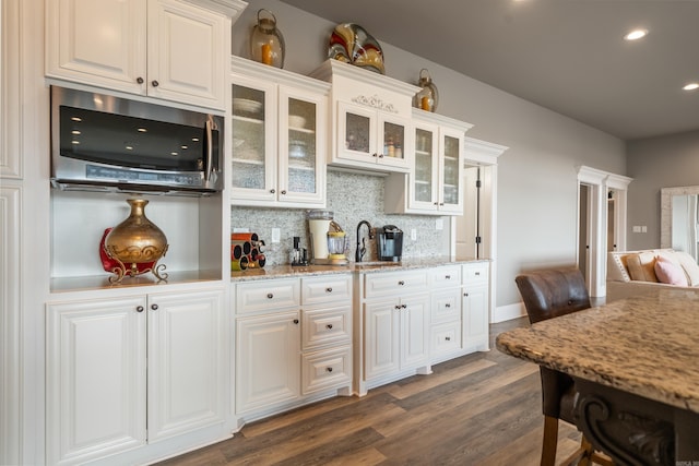 kitchen featuring decorative backsplash, dark wood-style flooring, stainless steel microwave, white cabinets, and glass insert cabinets