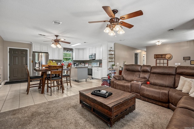 living area with a ceiling fan, light tile patterned floors, and a textured ceiling