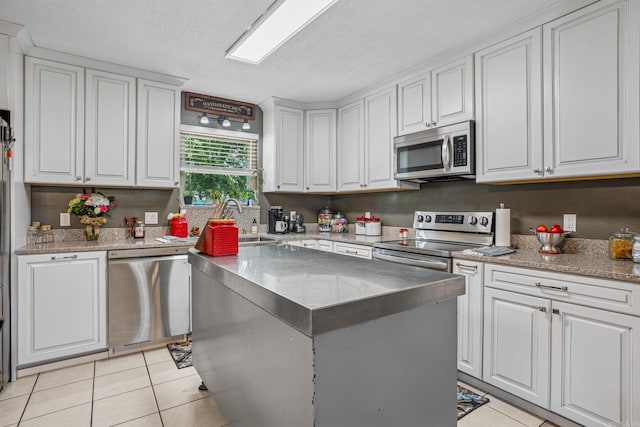 kitchen with stainless steel appliances, light tile patterned flooring, white cabinets, and a textured ceiling