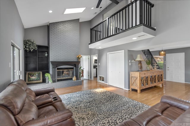 38 Ninth Fairway Loop, Maumelle, AR 72113 - living area with wood finished floors, high vaulted ceiling, a brick fireplace, stairway, and a skylight