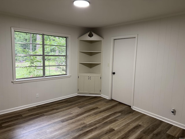 spare room with dark wood-style flooring, crown molding, baseboards, and built in shelves