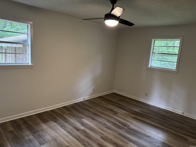 unfurnished room with a textured ceiling, healthy amount of natural light, dark wood-style floors, a ceiling fan, and baseboards