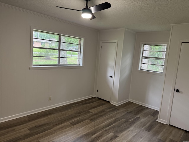 unfurnished bedroom with a textured ceiling, dark wood-type flooring, ornamental molding, a ceiling fan, and baseboards