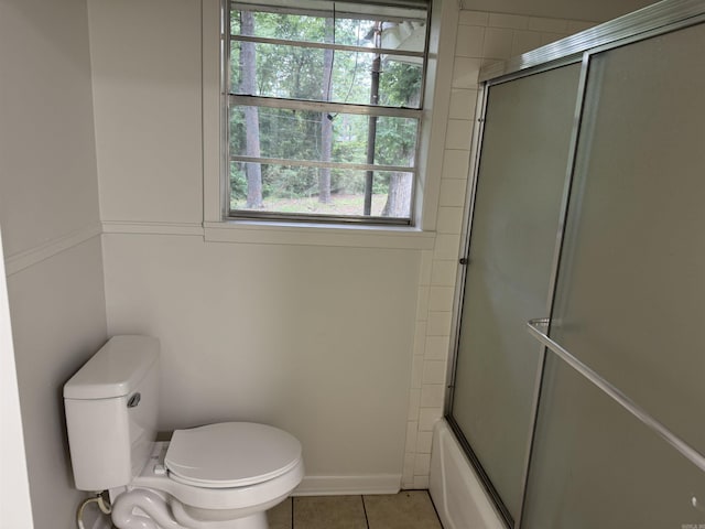 bathroom with toilet, tile patterned flooring, and bath / shower combo with glass door