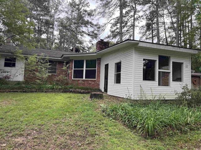 view of side of home with a chimney, a yard, and brick siding