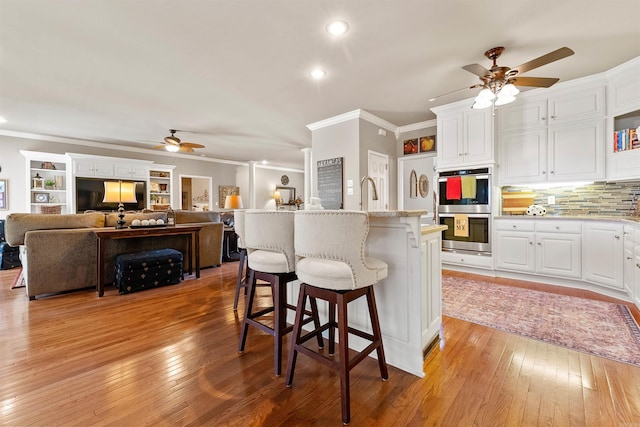 3305 Seminole Trl, Sherwood, AR 72120 - kitchen with a ceiling fan, double oven, ornamental molding, light wood-style floors, and white cabinets